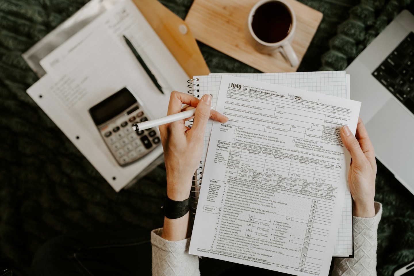 Hands reviewing a tax form with a pen, laptop, and calculator.